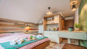 A bedroom with a bed, a bench, a small table, and a kitchenette. - Lukec Homestead Adventure Studio Meta, Kostel, Slovenia (Kostel)