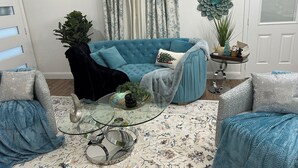 A living room with a blue sofa, a black chair, a glass coffee table, and a patterned rug.