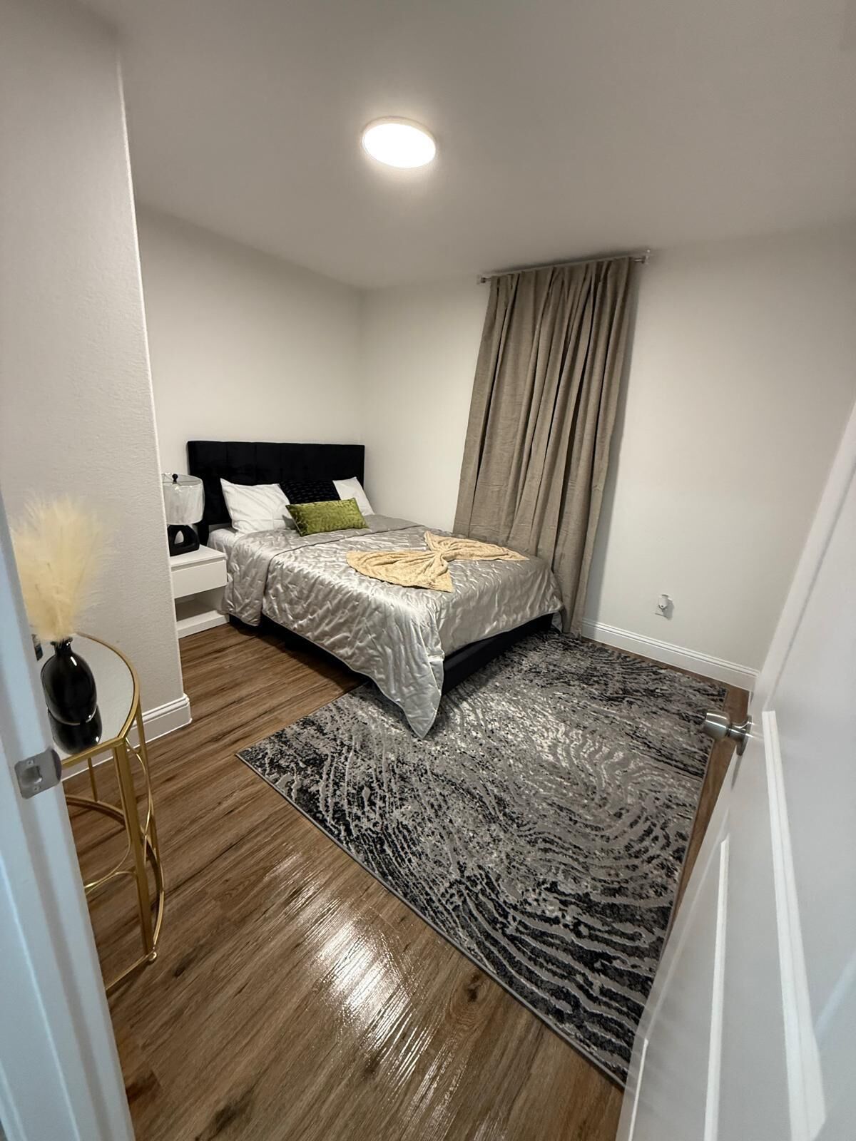 Quarto com cama, mesa de cabeceira, abajur, vaso e tapete.