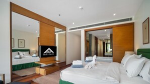 A modern hotel room with a large bed, a TV, and a bathroom visible through an open door. - Surin 2BR Resort Condo With Seaview@chava (Choeng Thale)