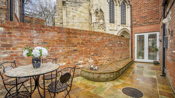 A courtyard with a round table and chairs, a brick wall, and a stone floor. - Micklegate Hideaway  -  Sleeps 4 Guests  in 2 Bedrooms (York)