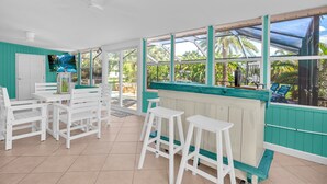 Eine helle, offene Terrasse mit weißer Möbel und einer wandfarben türkisen Wand.