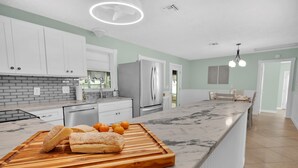 Eine moderne Küche mit weißen Schränken, einer Marmorarbeitsplatte und einem Holztisch mit Brot und Orangen.