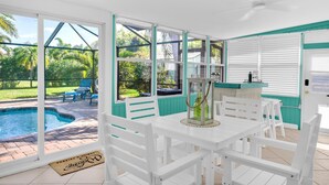 Eine überdachte Terrasse mit Pool, weißen Möbeln und Blick auf den Garten.