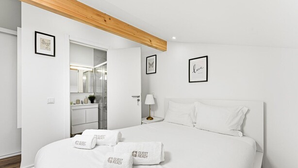 Una habitación de hotel moderna con una cama grande, ropa de cama blanca y un letrero que dice 'GUEST READY'.