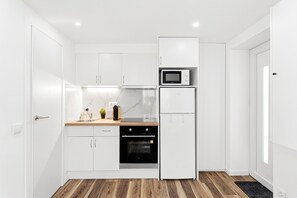 A compact kitchen with white cabinets, a microwave, a refrigerator, and a built-in oven.