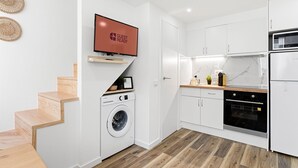 Una cocina moderna con armarios blancos, lavadora integrada, televisor de pantalla plana y una escalera de madera.