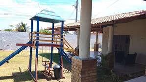 A playground with a blue and yellow climbing structure, a brick wall, and a covered seating area with chairs.