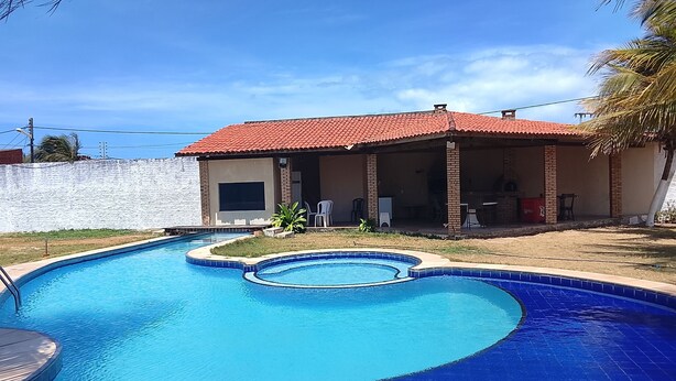 A swimming pool with a curved design, a covered patio area, and a brick building with a red roof.