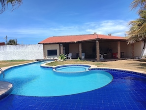 En pool med en böjd design, en täckt uteplats och en byggnad i tegel med ett rött tak.