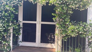 A covered entrance with a white door, surrounded by lush greenery and white flowers. - Private Estate with Main Heritage House + Cottages — Exclusive Use (Coochiemudlo Island)