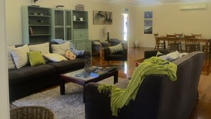 A living room with a sofa, armchairs, a coffee table, and a dining area with a table and chairs. - Private Estate with Main Heritage House + Cottages — Exclusive Use (Coochiemudlo Island)