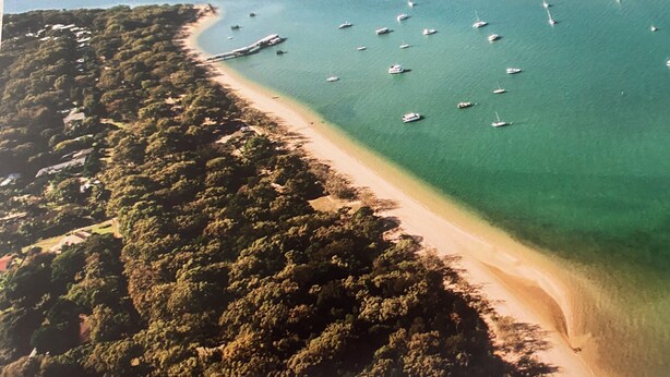 An aerial view of a beach with clear turquoise waters, numerous boats, and dense greenery along the coastline. - Private Estate with Main Heritage House + Cottages — Exclusive Use (Coochiemudlo Island)