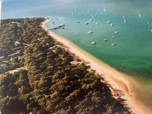 Luchtbeeld van een strand met helder turquoise water, diverse boten en weelderige begroeiing langs de kust.