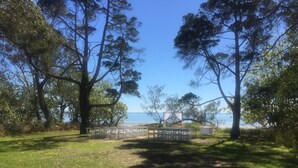 A grassy outdoor area with a seating arrangement and a view of the sea. - Private Estate with Main Heritage House + Cottages — Exclusive Use (Coochiemudlo Island)