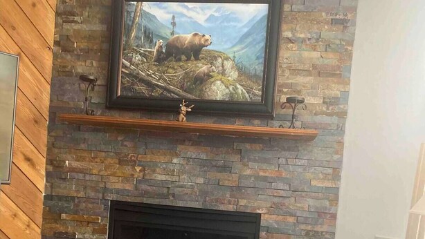 Ein Wohnzimmer mit Kamin aus Stein, einem darüber hängenden Fernseher und Holzboden.