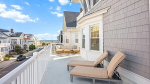 A balcony with two lounge chairs, a white railing, and a view of the street and ocean. - 6BR Beach Block Paradise - Ocean Views - Sleeps 20 (Ventnor City)