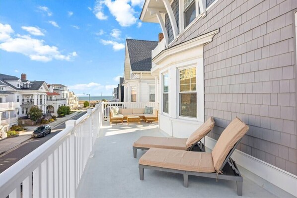 A balcony with two lounge chairs, a white railing, and a view of the street and ocean.