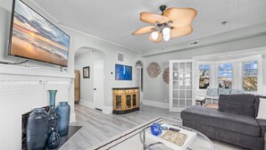 A spacious living room with a large flat-screen TV, a grey sofa, a coffee table, and a ceiling fan. - 6BR Beach Block Paradise - Ocean Views - Sleeps 20 (Ventnor City)