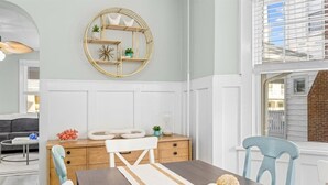 A dining area with a wooden table, white chairs, and a round gold-framed shelf with decorative items. - 6BR Beach Block Paradise - Ocean Views - Sleeps 20 (Ventnor City)