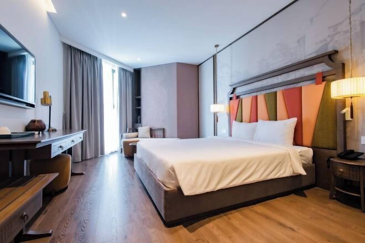 A modern hotel room with a large bed, a desk, a TV, and a view of the city.