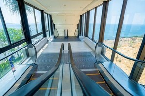 Ein Innenbereich mit Rolltreppen, großen Fenstern und Blick auf den Strand.