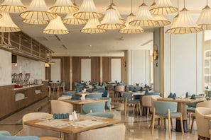 Un restaurant doté de nombreuses tables et chaises, d’un bar et d’un éclairage suspendu.