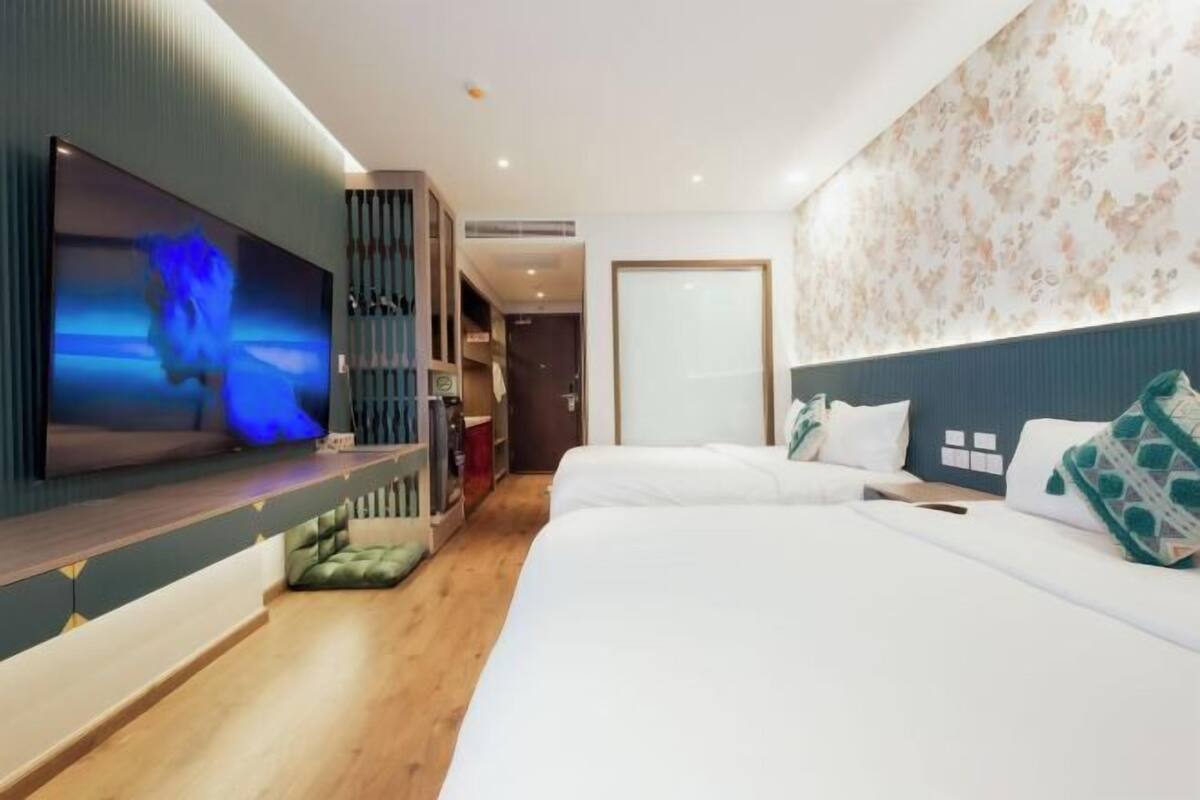 A hotel room with a TV, two beds, a wardrobe, and a floral wall.