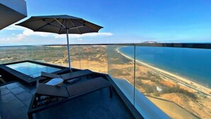 Un balcon situé dans un immeuble de grande hauteur, doté d’une rambarde en verre, qui offre une vue sur un paysage côtier.