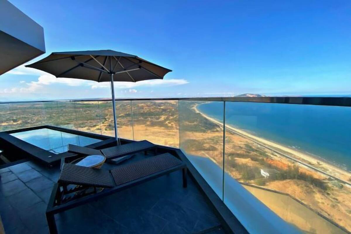 A high-rise balcony with a glass railing overlooking a coastal landscape.