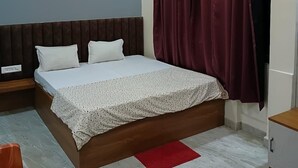 A modern bedroom with a bed, a nightstand, a red rug, and a ceiling fan. - Hotel Keshav (Savner)