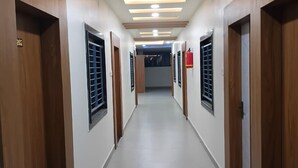 A hallway with wooden doors, recessed lighting, and a tiled floor. - Hotel Keshav (Savner)