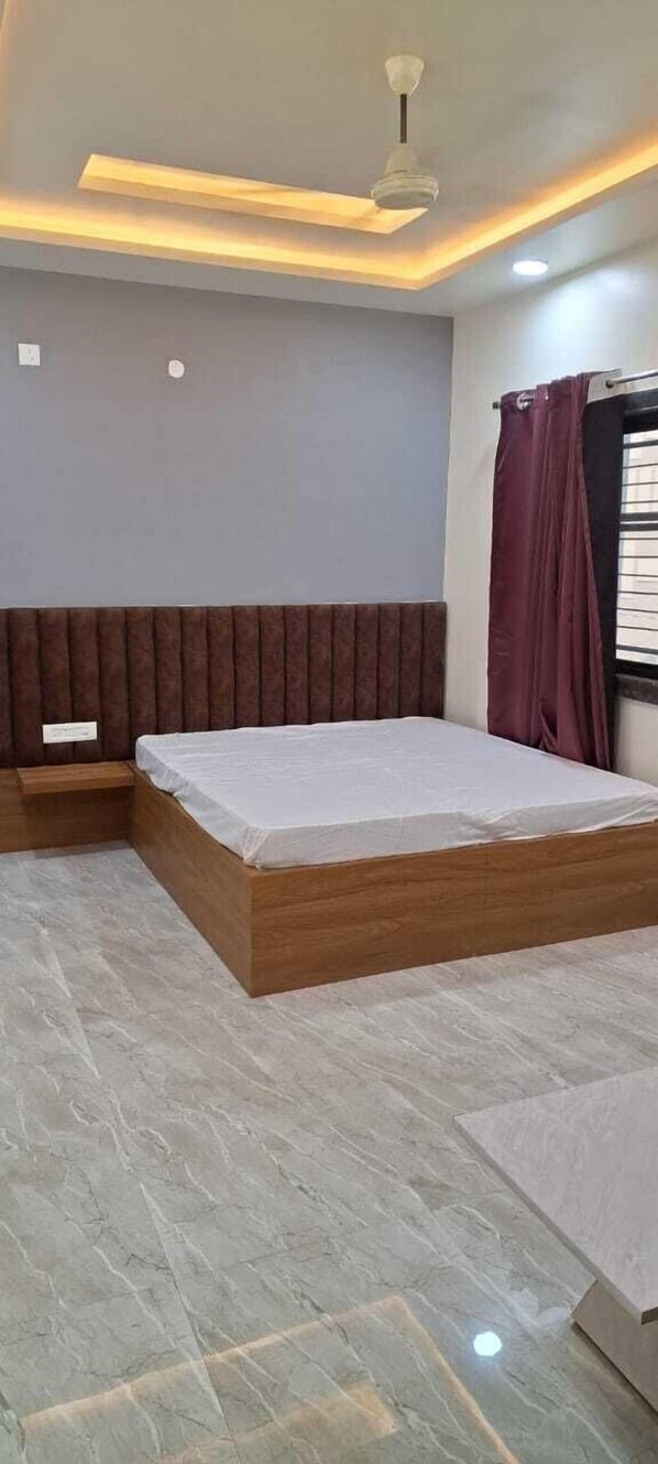 A modern bedroom with a wooden bed, a built-in bench, and a ceiling fan. - Hotel Keshav (Savner)