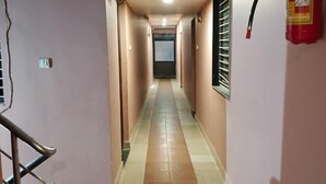 A hallway with a fire extinguisher mounted on the wall, a handrail, and a tiled floor. - Hotel Keshav (Savner)