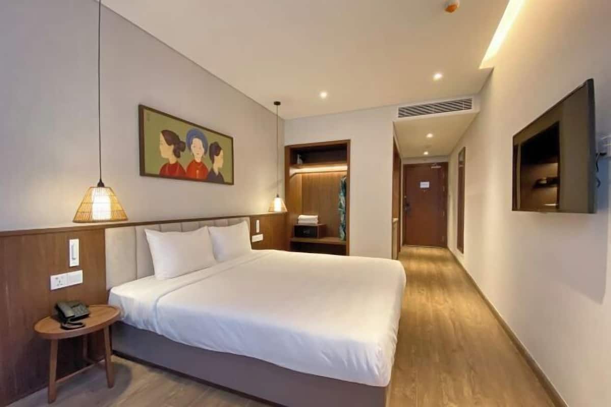 Una habitación de hotel con una cama grande, lámparas de noche, un cuadro en la pared, un televisor montado y suelo de madera.