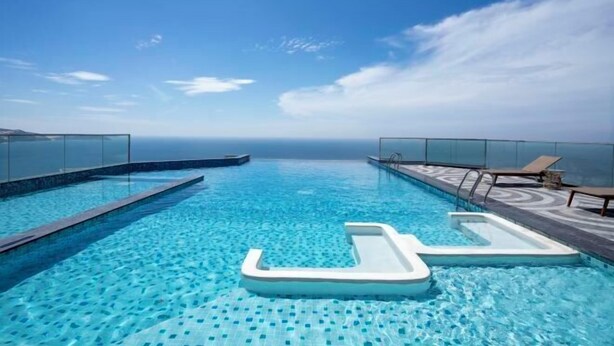 A rooftop infinity pool with clear blue water, lounge chairs, and a glass barrier. - Couple & Co. Boutique Mandala (Phan Thiet)