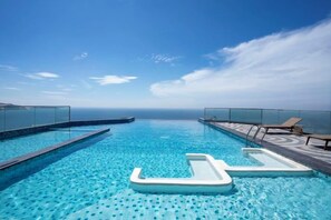A rooftop infinity pool with clear blue water, lounge chairs, and a glass barrier. - Couple & Co. Boutique Mandala (Phan Thiet)