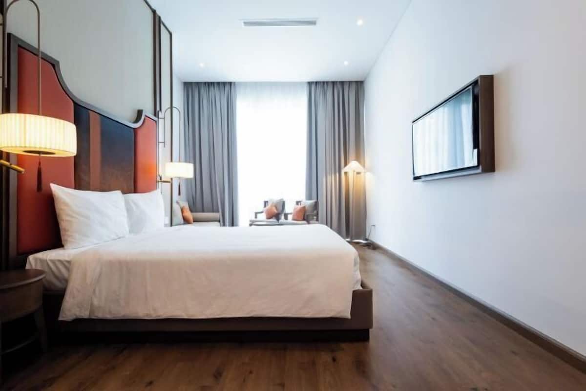 Habitación de hotel con una cama grande, dos lámparas de noche, un televisor en la pared y vistas al exterior a través de la ventana.