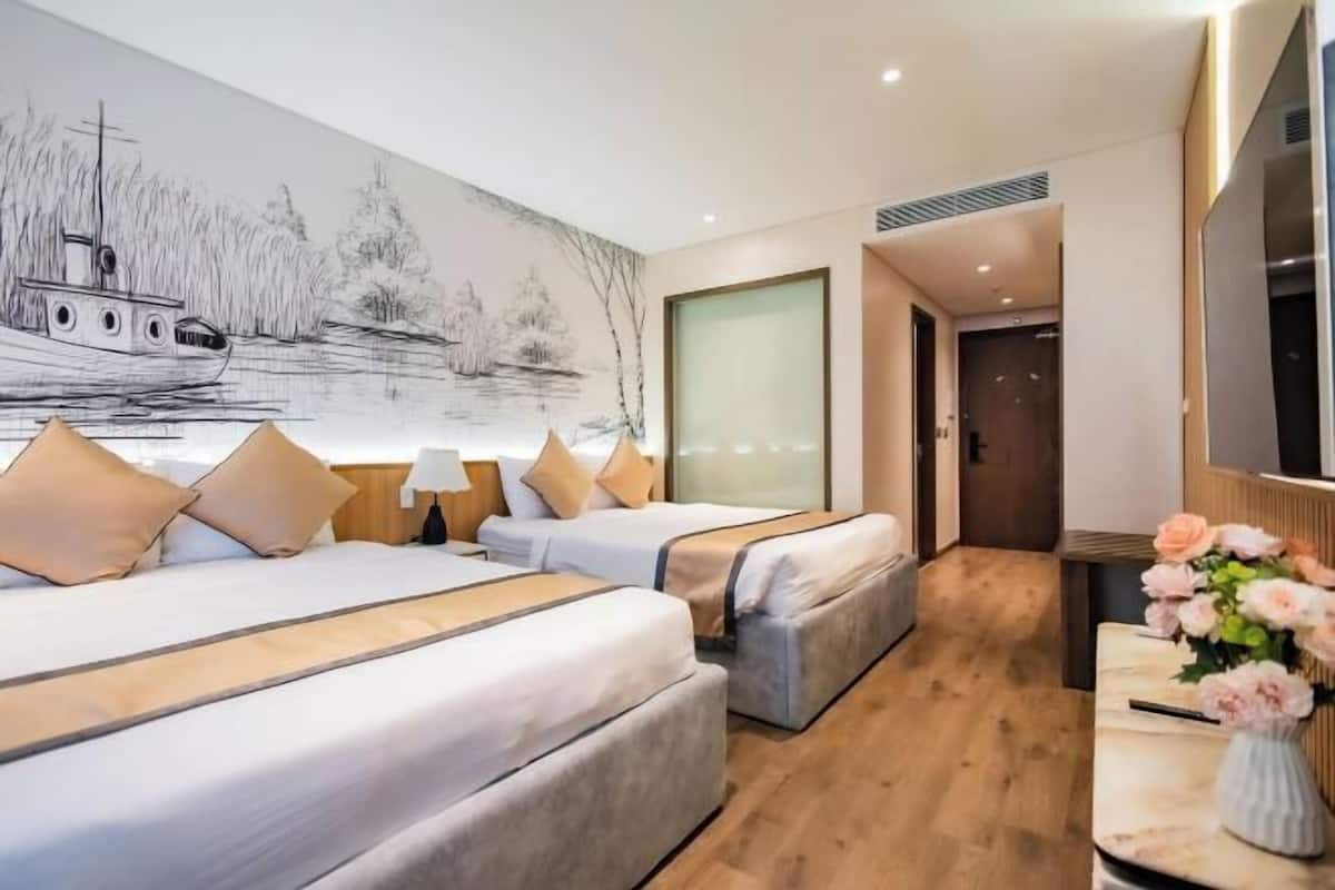 Habitación de hotel con dos camas, un cuadro grande de un barco en la pared, piso de madera y un jarrón con flores sobre una mesa.