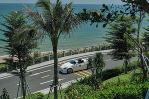 A white convertible car driving on a road with a view of the ocean and palm trees. - Couple & Co. Boutique Mandala (Phan Thiet)