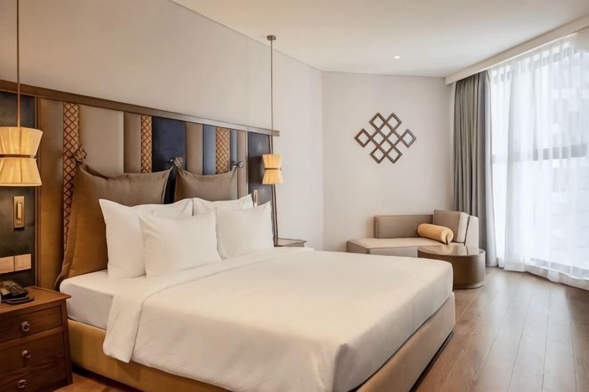 A hotel room with a large bed, bedside tables, a chair, and a window with curtains.