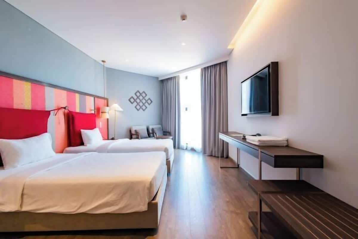 Habitación de hotel con dos camas, un escritorio, un televisor y una ventana con cortinas.