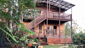Ein zweistöckiges Holzhaus mit einem Balkon, umgeben von üppiger Vegetation und einem gepflegten Garten.