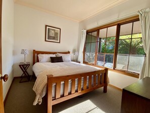Ein Schlafzimmer mit einem hölzernen Bett, einem Nachttisch, einem gerahmten Bild an der Wand und einem großen Fenster mit Vorhängen.