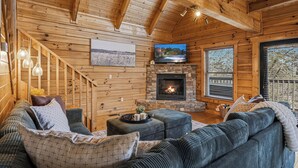 A cozy log cabin interior with a fireplace, a large TV, and a comfortable seating area. - Cozy Log Cabin - Hot Tub, Games, & Mountain Views (Sevierville)