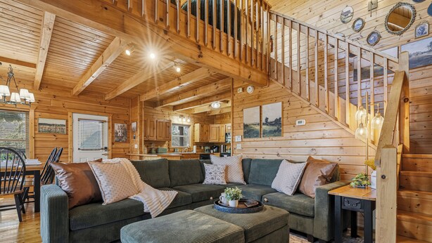 A cozy cabin interior with a wooden staircase, a large sectional sofa, and a dining area. - Cozy Log Cabin - Hot Tub, Games, & Mountain Views (Sevierville)