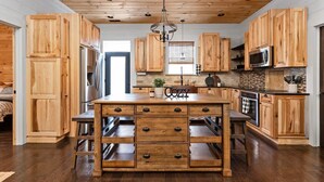 Una cocina con armarios de madera, una isla central con cajones, una lámpara colgante y un microondas.