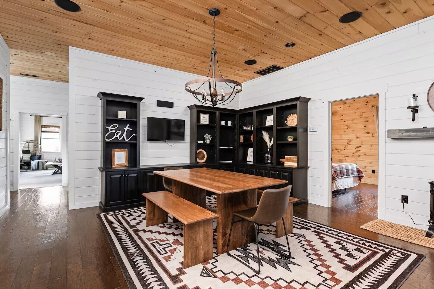 A modern kitchen with a wooden table, black cabinets, and a patterned rug.
