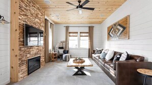 Una sala de estar moderna con chimenea, techo de madera y un amplio sofá de cuero marrón.