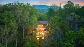 A lodge surrounded by dense forest with a view of mountains in the background. - The Highland • Fabulous 9BR Gatlinburg Cabin With Mountain Views (Gatlinburg)